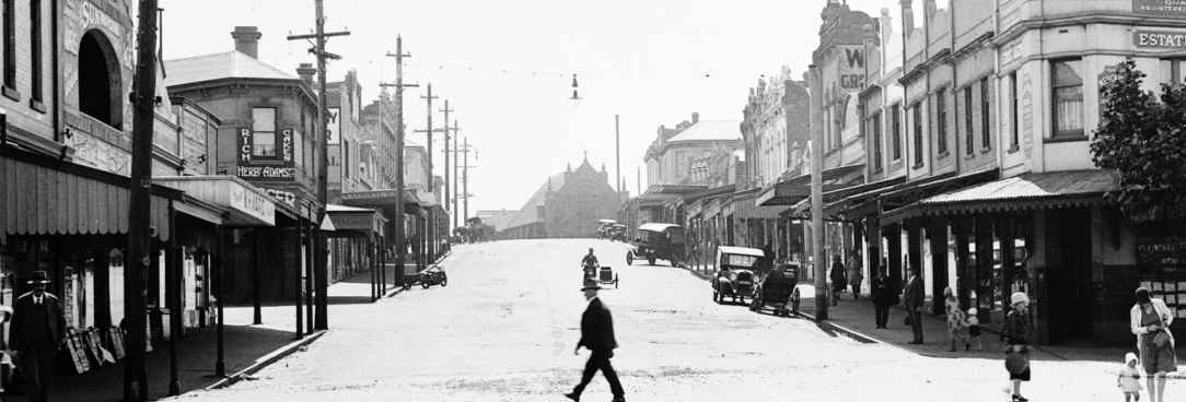 Street scene Macaualay Road Kensington looking west from railway gates, VPRS 12800/P3, ADV/0473 Black and white photo of a suburban street