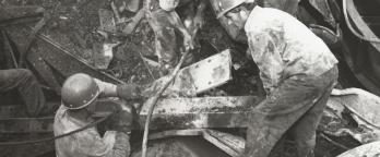 Black and white photo, rescuers searching through the rubble for survivors after the bridge collapse.