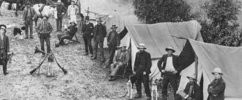 A black and white image of soldier settlers amidst tents on farming land
