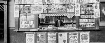 Black and white image of man working at newspaper stand, Spencer St train station